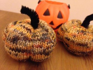 2 knitted pumpkins and a small plastic pumpkin pot
